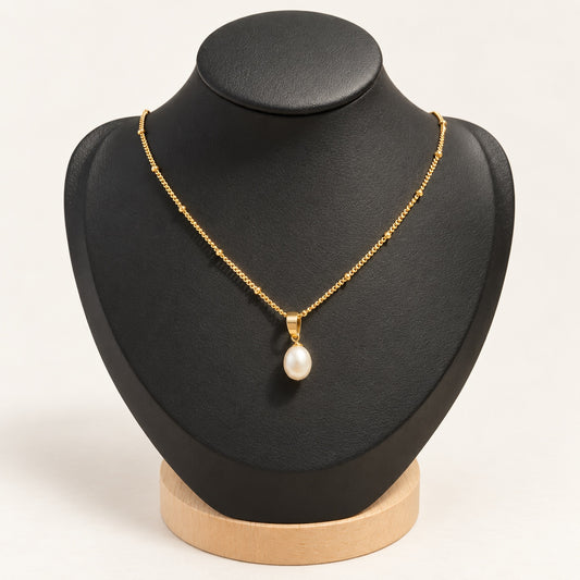 Collier doré avec perle d’eau douce sur présentoir noir, fond clair