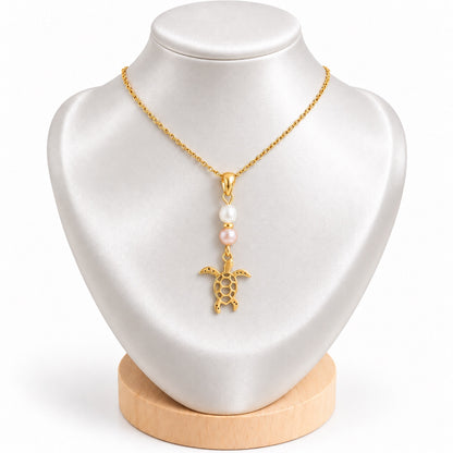 Collier tortue doré avec perles d’eau douce blanche et rosée sur présentoir blanc satiné
